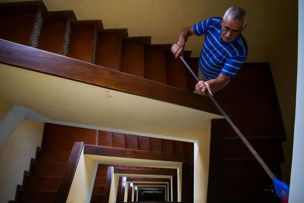 An elderly man cleaning an indoor staircase with a mop, showcasing everyday life and work.
